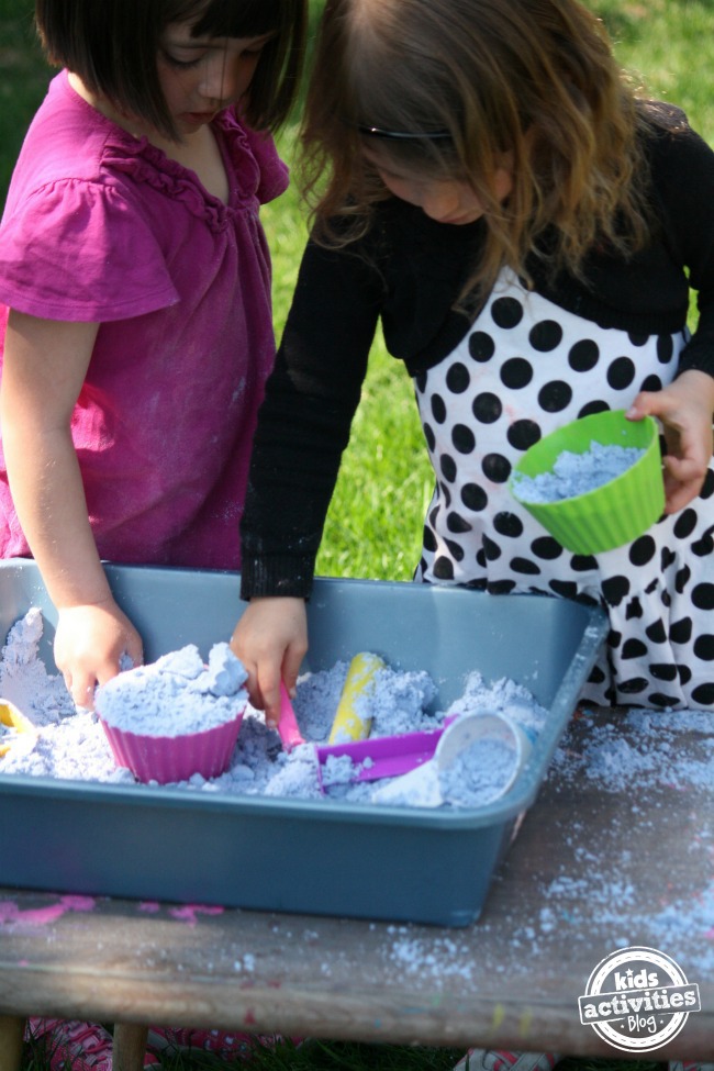 Toddler-Safe Cloud Dough turned into a sensory bin with silicone cup cake molds, cups, shovels, and sticks.