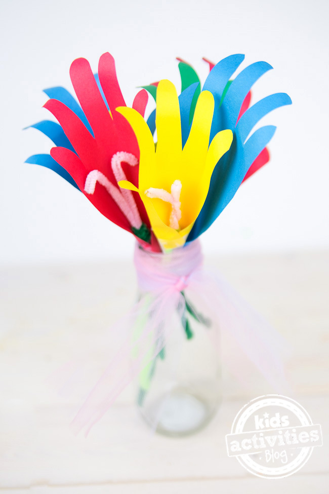 Handprint flower craft made of red, blue, yellow construction paper with green pipe cleaners as stems.