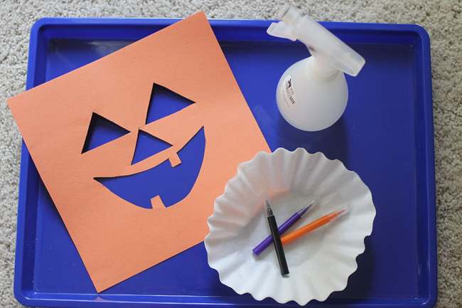 Halloween Jack-O-Lantern Art Project for Kids with orange construction paper with a jack o lantern face cut out, coffee filter, markers, and a spray bottle.