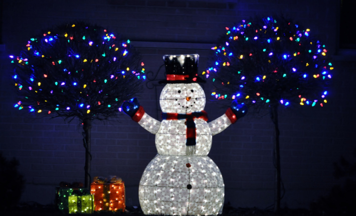 Lit snowman for the holidays with Christmas lights of many colors behind him found on light scavenger hunt printed from Kids activities blog