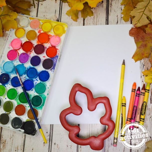 Paints, leaves cookie cutters, pencils, paper, and crayons about to make warhol inspired fall leaf art project.