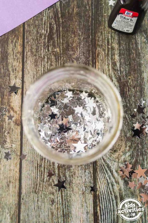 A mason jar filled with a few tablespoons of silver star confetti. 