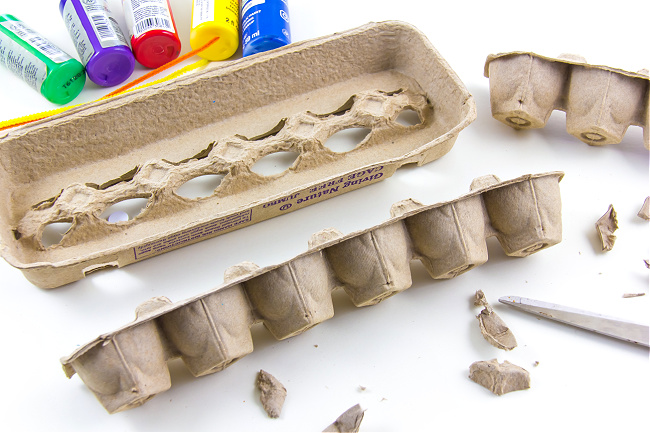 A brown egg carton being cut in half to make egg carton caterpillars