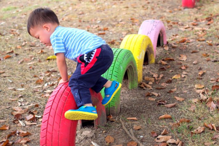 physical development 2 year old - boy jumping over tires outside with colorful tires - red, green, yellow and pink
