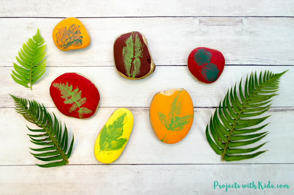 Painted rocks with leaf stamps on them from Projects with Kids - fern leaves shown with multiple colored rocks stamped with fall leaves