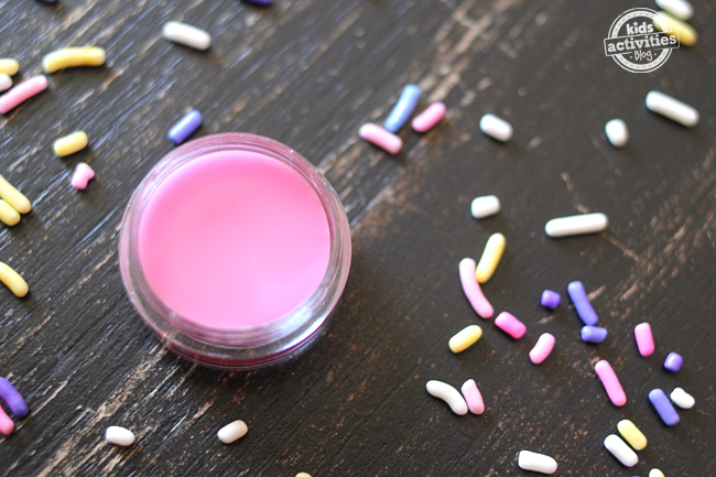 pink lip balm in a circle container surrounded by sprinkles.