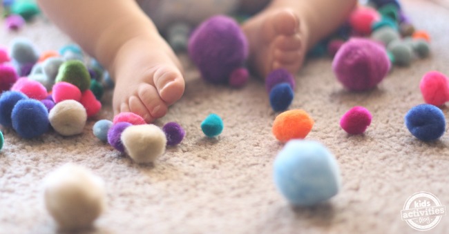 1 year old playing with pom poms on the floor - feet and pom poms showing