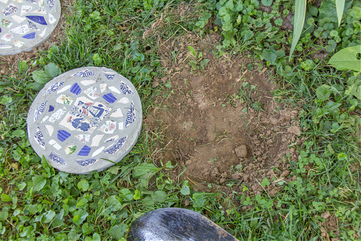 A shallow round hole dug in the ground to put a concrete stepping stone inside.