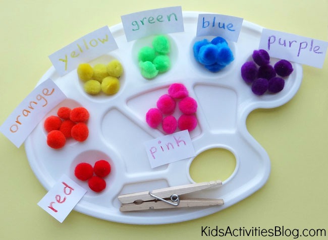 Color sorting game for preschoolers using red, orange, yellow, green, blue, and purple pom poms with clothes pins and paint palettes.