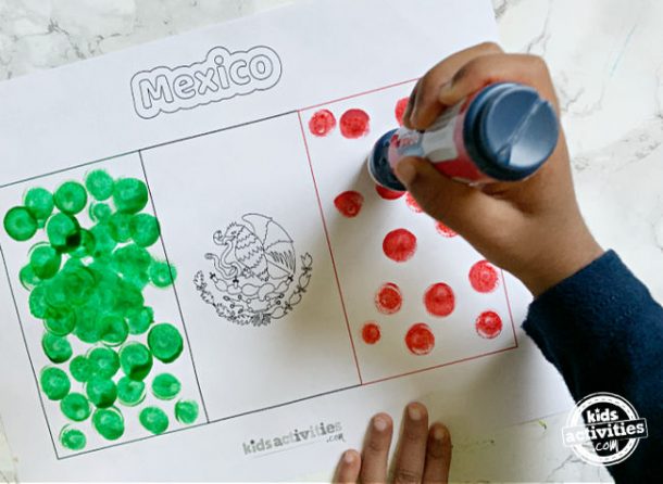 Toddler holding dot maker and making dots to complete mexican flag activity