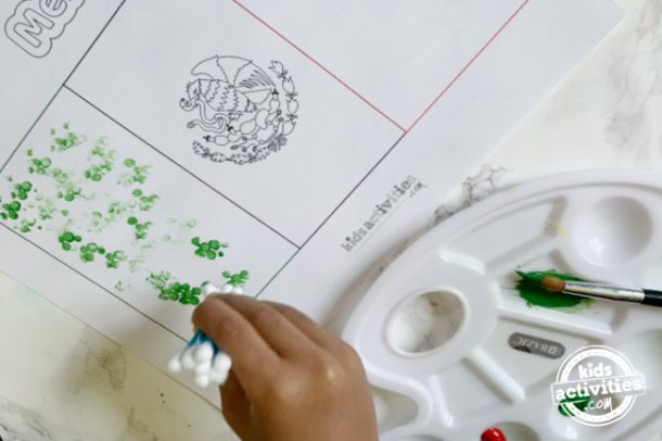 a toddler using ear buds to make dots to fill the mexican flag in corresponding colors
