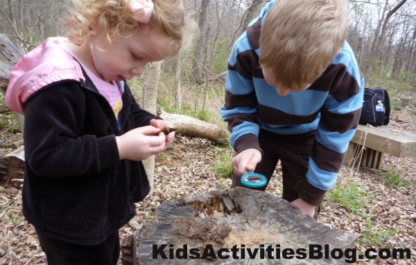 kids exploring in woods on Earth Day April 22 - two kids looking at a stump with magnifying glass