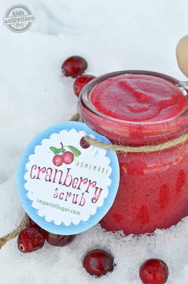 DIY sugar scrub that is made of cranberries, in a jar, with a cranberry scrub tag, in the snow.