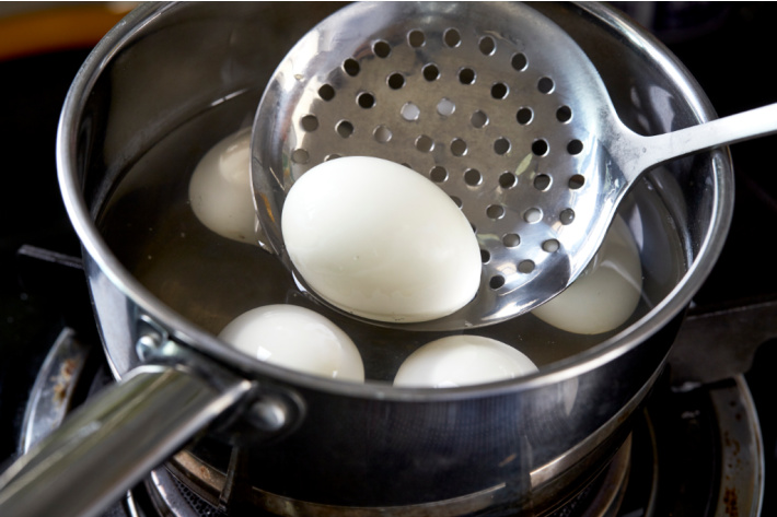 Boiling eggs in preparation for Easter egg dyeing - Kids Activities Blog - eggs shown in pan with slotted spoon to get egg out