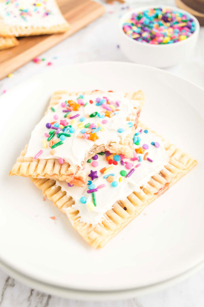 Two homemade pop tarts topped with white frosting and colorful sprinkles sitting on a white plate.