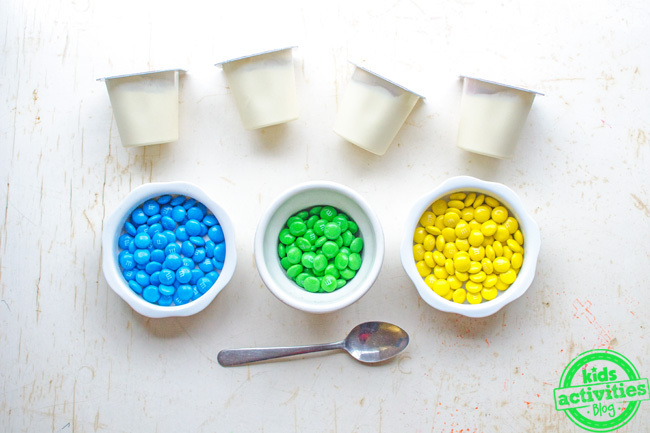 yellow and blue make green snack idea - four vanilla pudding cups shown with candies in bowls of blue yellow and green