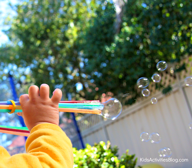 small child using a bubble shooter wand to blow bubbles across the backyard fence