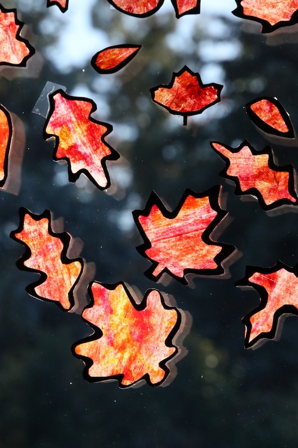 autumn leaf suncatcher craft for kids shown with orange yellow and red leaves on a window from Happy Hooligans