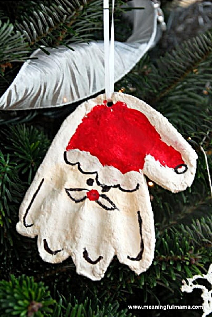 Handprint santa ornament where the fingers are Santa's beard hanging on a tree.