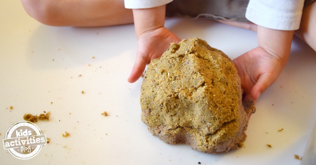 Homemade Kinetic sand recipe that uses play sand and slime that is being mixed by the hands of a child.