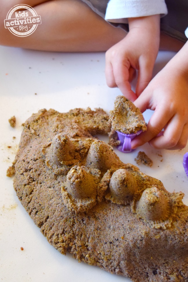 DIY kinetic sand made with slime and paly sand. It is being played with using purple plastic toys by little hands.