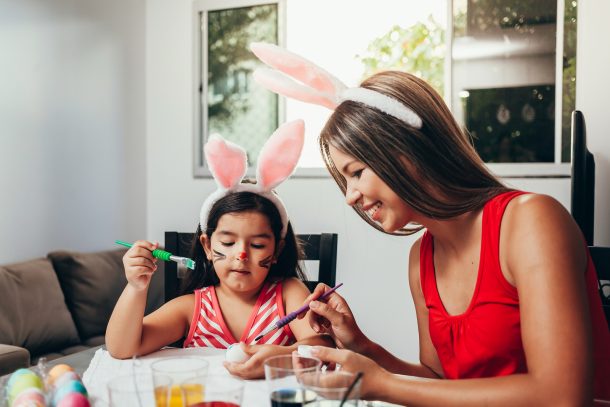 A mom and daughter with bunny ears painting Easter Egg decorations on boiled eggs.